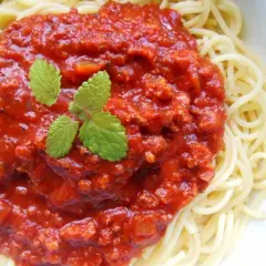 Spaghetti z bogatym sosem pomidorowym i mięsem mielonym, udekorowane listkami mięty.