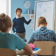 Nauczyciel tłumaczy coś dzieciom w klasie. Zastanawiasz się, ile zarabia nauczyciel klas 1-3?