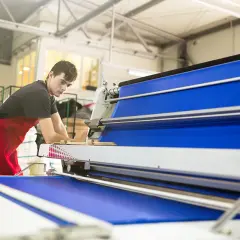 Un homme en tablier rouge travaille sur une machine textile bleue.