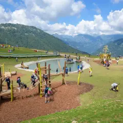 Un'area giochi con un laghetto e un galeone, dove tante famiglie si divertono in montagna con i bambini.