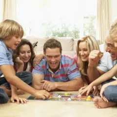 Familie spielt ein kooperatives Brettspiel, lachend und konzentriert auf dem Boden liegend.
