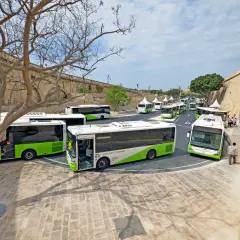 Autobusy Malta Public Transport czekają na pasażerów. Wiele zielono-białych pojazdów ustawionych w rzędzie, gotowych do odjazdu z okolic lotniska.