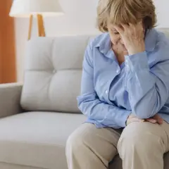 Femme âgée assise sur un canapé, la main sur le front, évoquant la recherche d'un hypotension traitement naturel.