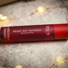 En röd flaska med IDUN Minerals Ready Set Refresh Setting Spray ligger bland julbelysning.