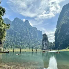 Khao Sok Nationalpark: Majestätische Kalksteinfelsen ragen aus einem ruhigen See empor, umgeben von üppigem Dschungel. Ein Boot gleitet über das Wasser.