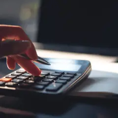 Dłoń z długopisem naciska klawisze kalkulatora, licząc, ile zarabia 1% najbogatszych Polaków. Obok leży otwarty notatnik i laptop.