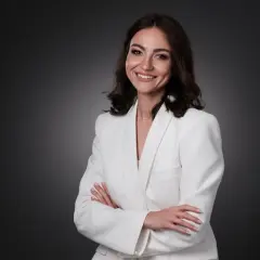 Uśmiechnięta kobieta w białej marynarce, z rękami skrzyżowanymi na piersi. Idealna sesja biznesowa pozy.
