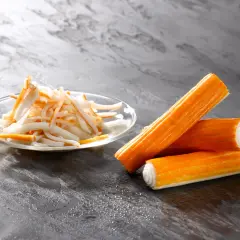 Surimi co to? Pomarańczowe paluszki i pokrojone w słupki surimi na talerzyku.