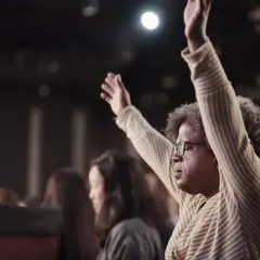 Frau mit erhobenen Armen in einer Kirche, die eine Atmosphäre der Anbetung widerspiegelt, die manche als Kritik an der Bethel Church sehen.