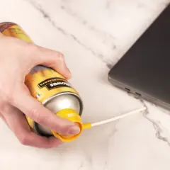 Main d'une personne utilisant une bombe d'air comprimé pour nettoyer un ordinateur portable.