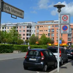 Ulica w Niemczech z kolorowymi kamienicami, znakami drogowymi (w tym fotoradary w niemczech) i zaparkowanymi samochodami.