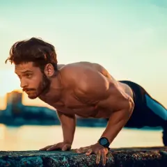 Mężczyzna wykonuje pompki na biceps przy zachodzie słońca nad wodą.