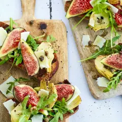 Tartines de pain grillé garnies de figues fraîches, d'artichauts, de roquette et de copeaux de parmesan.