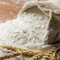 Wsypana z worka mąka pszenna i kłosy zbóż. To właśnie z nich powstaje gluten, kluczowy składnik wypieków.