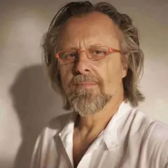 Portret mężczyzny w okularach, jednego z polskich kompozytorów współczesnych, z siwiejącą brodą i włosami, w białej koszuli.