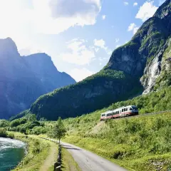 Ein Zug fährt durch eine malerische Berglandschaft. Ein perfekter Urlaub mit dem Zug, vorbei an einem Fluss und grünen Hängen.