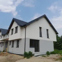 Nowy, dwukondygnacyjny dom w budowie, z szarym dachem i dwukolorową elewacją. To może być najtańszy dom w budowie do 100m.