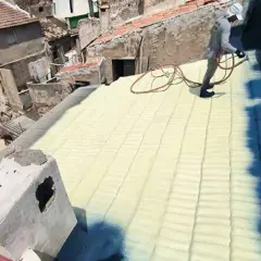 Trabajador aplica aislamiento con poliuretano en un tejado. La espuma amarilla cubre las tejas, creando una capa protectora.