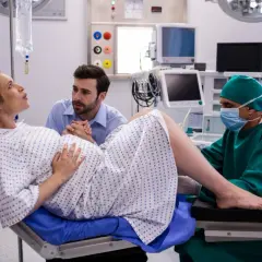 Kobieta w ciąży na fotelu porodowym, wspierana przez partnera i lekarza.