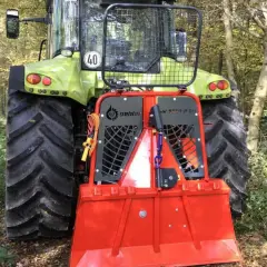 Ein grüner Traktor mit einem roten Forstkran im Wald.