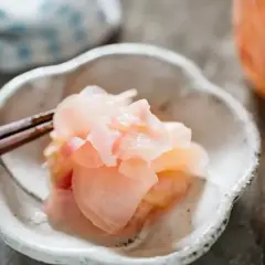 Różowy imbir do sushi, delikatnie podany na talerzyku z pałeczkami. Idealny dodatek do każdego sushi.