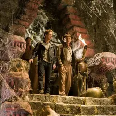 Indiana Jones i Królestwo Kryształowej Czaszki obsada: Indiana z pochodnią i Mutt na schodach w pajęczynach, obok kamiennych głów.