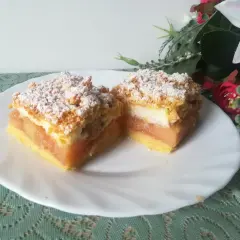 Dwa kawałki szarlotki z bezą i kruszonką, posypane cukrem pudrem, na białym talerzu.
