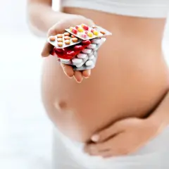 Kobieta w ciąży trzyma w dłoni opakowania leków przeciwbólowych.