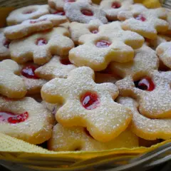 Koszyczek pełen pysznych, kruchych ciasteczek babci, posypanych cukrem pudrem i z czerwonym dżemem w środku.