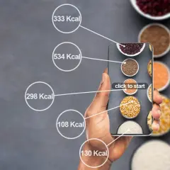 Dłoń trzyma smartfon z aplikacją do liczenia kalorii. Na ekranie widać różne produkty spożywcze i ich kaloryczność, pomocne przy diecie 1500 kcal.