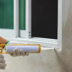 Ręka w rękawicy uszczelnia okno akrylem na zewnątrz.