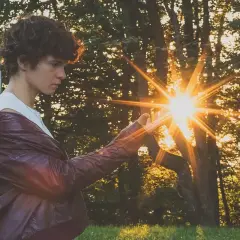 Chłopak w skórzanej kurtce łapie promienie zachodzącego słońca. Ciekawe fotografie z magicznym blaskiem.