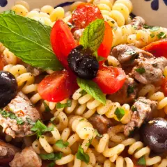 Pasta con pesce spada, pomodorini, olive nere e menta fresca in una ciotola decorata.