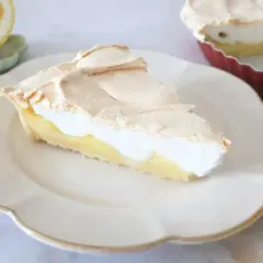 Pyszna tarta cytrynowa z puszystą bezą na wierzchu, podana na białym talerzu. Obok leży połówka cytryny.