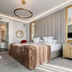 Elegancki pokój hotelowy 4-gwiazdkowy spełniający wysokie wymagania: łóżko z puszystym kocem, kryształowy żyrandol, złote lustra i stylowe meble.
