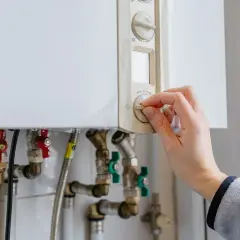 Main tenant ajuste le thermostat de sa chaudière à gaz. Une aide pour le changement de chaudière gaz est peut-être nécessaire.