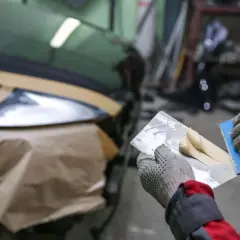 Ręce w rękawiczkach przygotowują masę do naprawy karoserii włóknem szklanym.