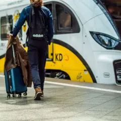Podróżny z walizką i kurtką idzie na pociąg. Może to być podróż z Warszawy do Gdyni.