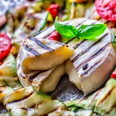 Co na grilla oprócz mięsa? Grillowany ser camembert z cukinią i pomidorami, udekorowany bazylią.