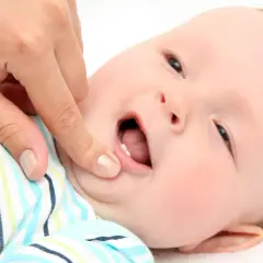 Dziecko z otwartymi ustami, któremu dorosły palcem sprawdza ząbkowanie. Widoczne pierwsze ząbki, nietypowe objawy ząbkowania mogą być łagodne.