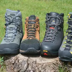 Four hiking boots, showcasing what boots are made of, sit on a log. Materials include leather, mesh, and rubber soles.