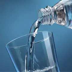 Un filet d'eau pure, riche en magnésium, se verse d'une bouteille dans un verre transparent sur fond bleu.