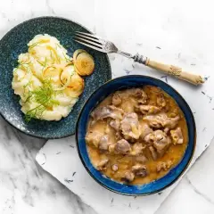 Gulasz z żołądków w kremowym sosie, podany z puree ziemniaczanym i karmelizowaną cebulką. Pyszne danie obiadowe.