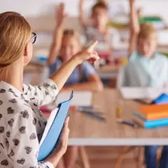 Nauczycielka w klasie z uczniami podnoszącymi ręce. Pokazuje, jak zostać nauczycielem przedmiotów zawodowych.