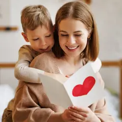 Chłopiec obejmuje mamę, która czyta kartkę z sercem. To piękna zagadka o mamie, pełna miłości.