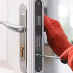 Main tenant utilise un tournevis pour changer la serrure d'une porte blanche.