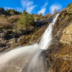 Cascada en un paisaje rocoso y seco, con vegetación escasa. El agua cae con fuerza, creando una estela blanca. Un rincón natural cerca de San Mamés, Madrid.