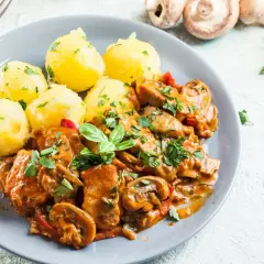 Pyszny gulasz z kurczaka z pieczarkami i papryką, podany z ziemniakami posypanymi natką pietruszki.