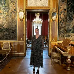 En kvinna står i en sal på Hallwylska museet Stockholm, omgiven av antika gobelänger, en flygel och utsökt inredning.
