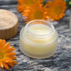 Zutaten für calendula creme selber machen: Ringelblumen, ein Glas mit Creme und ein Holzdeckel.